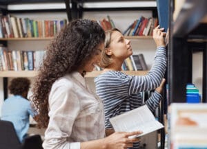 Two colleagues reaching for books on a library shelf
