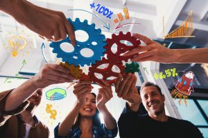 Hands assembling coloured gears over business sketches