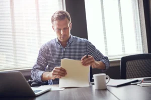 An internal quality assurer reviewing assessment records at a desk in a training provider office