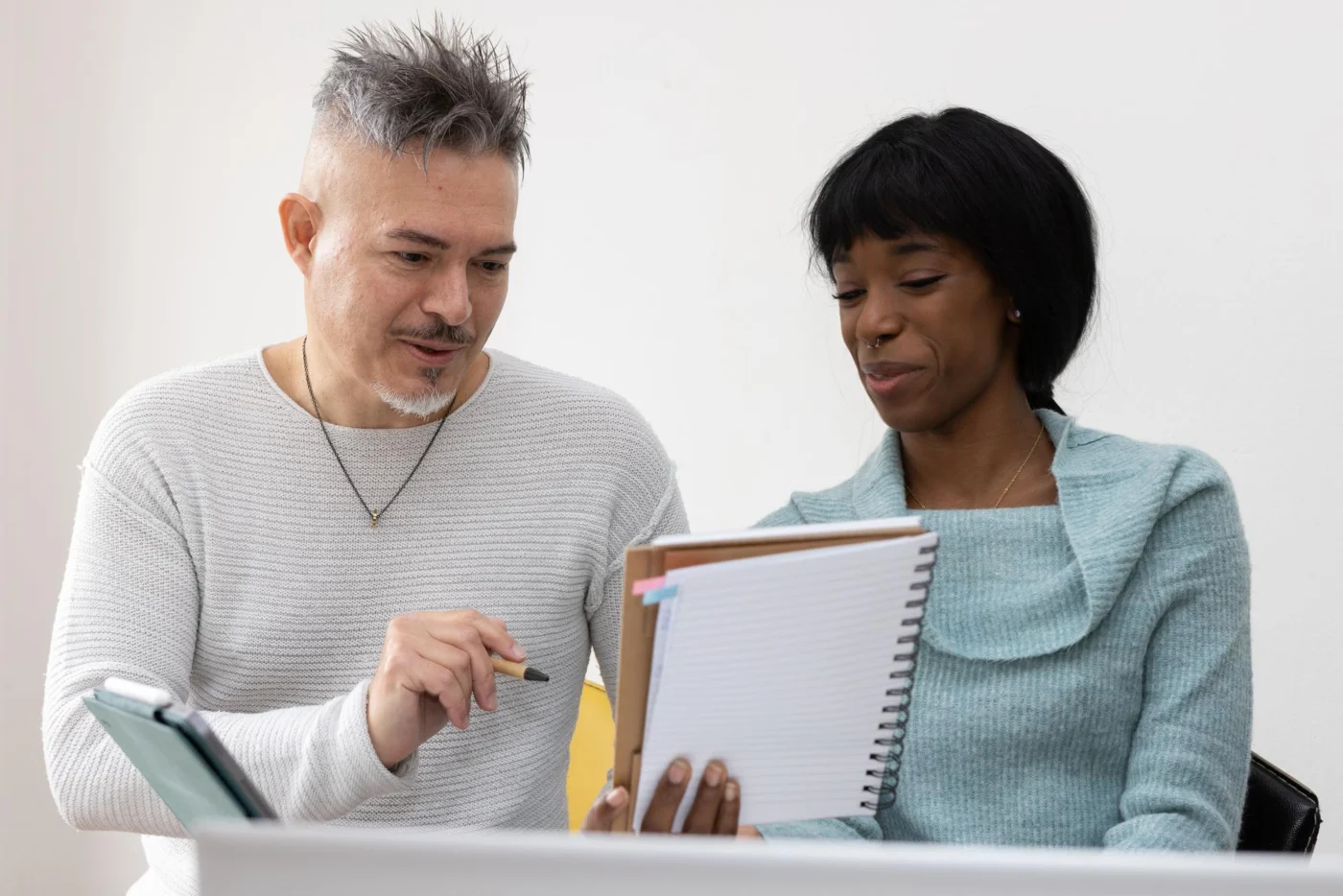 Two colleagues sitting together going through a notebook and paperwork at a desk