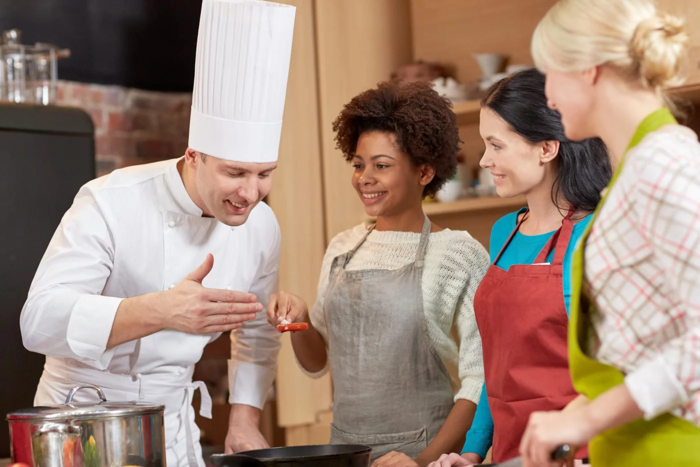 A chef demonstrating a technique to a group of adult learners in a training kitchen