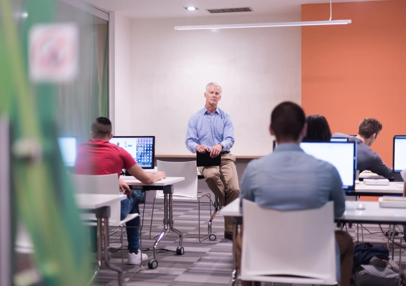 An experienced tutor at the front of a college IT suite while adult learners work at computers