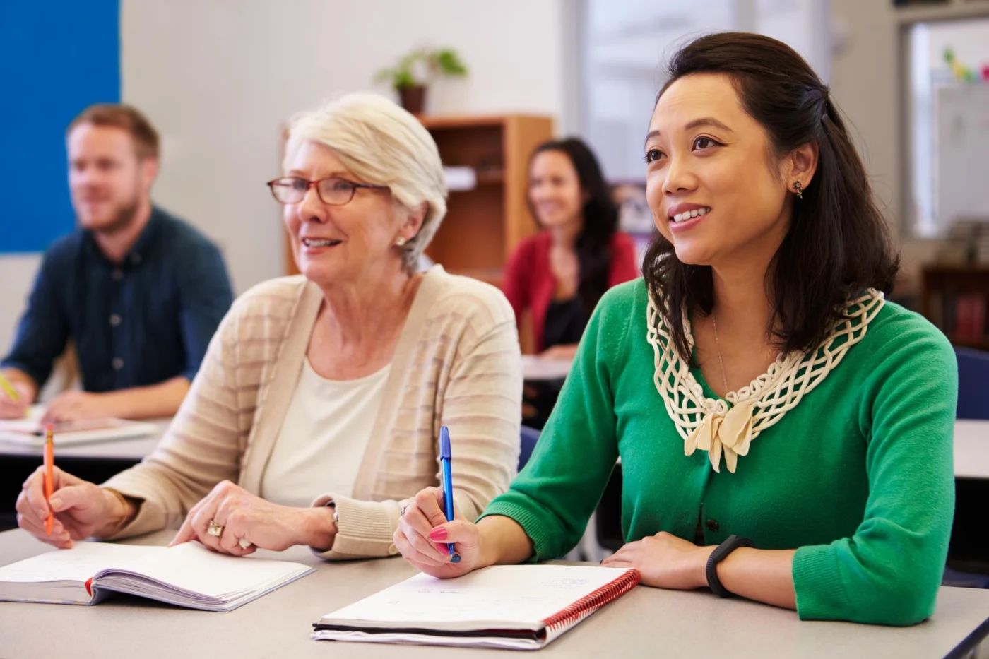 Two adult learners sharing a desk in an adult education class, looking up from their notebooks