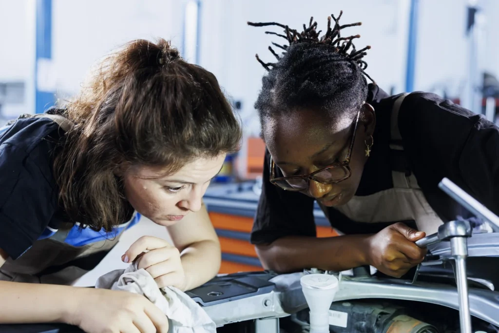 An adult technical tutor guiding post-16 students on real engineering equipment in a college workshop