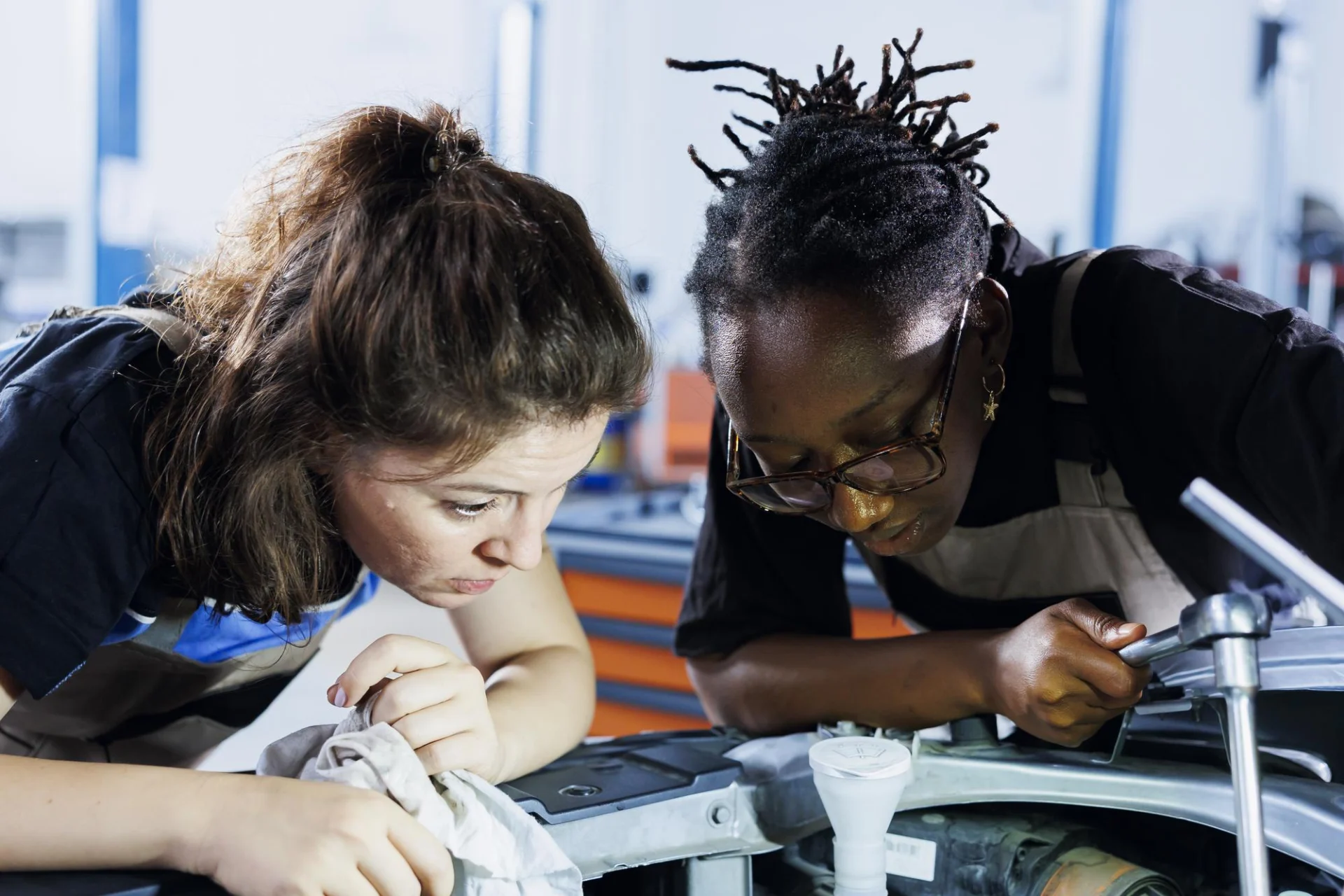 An adult technical tutor guiding post-16 students on real engineering equipment in a college workshop
