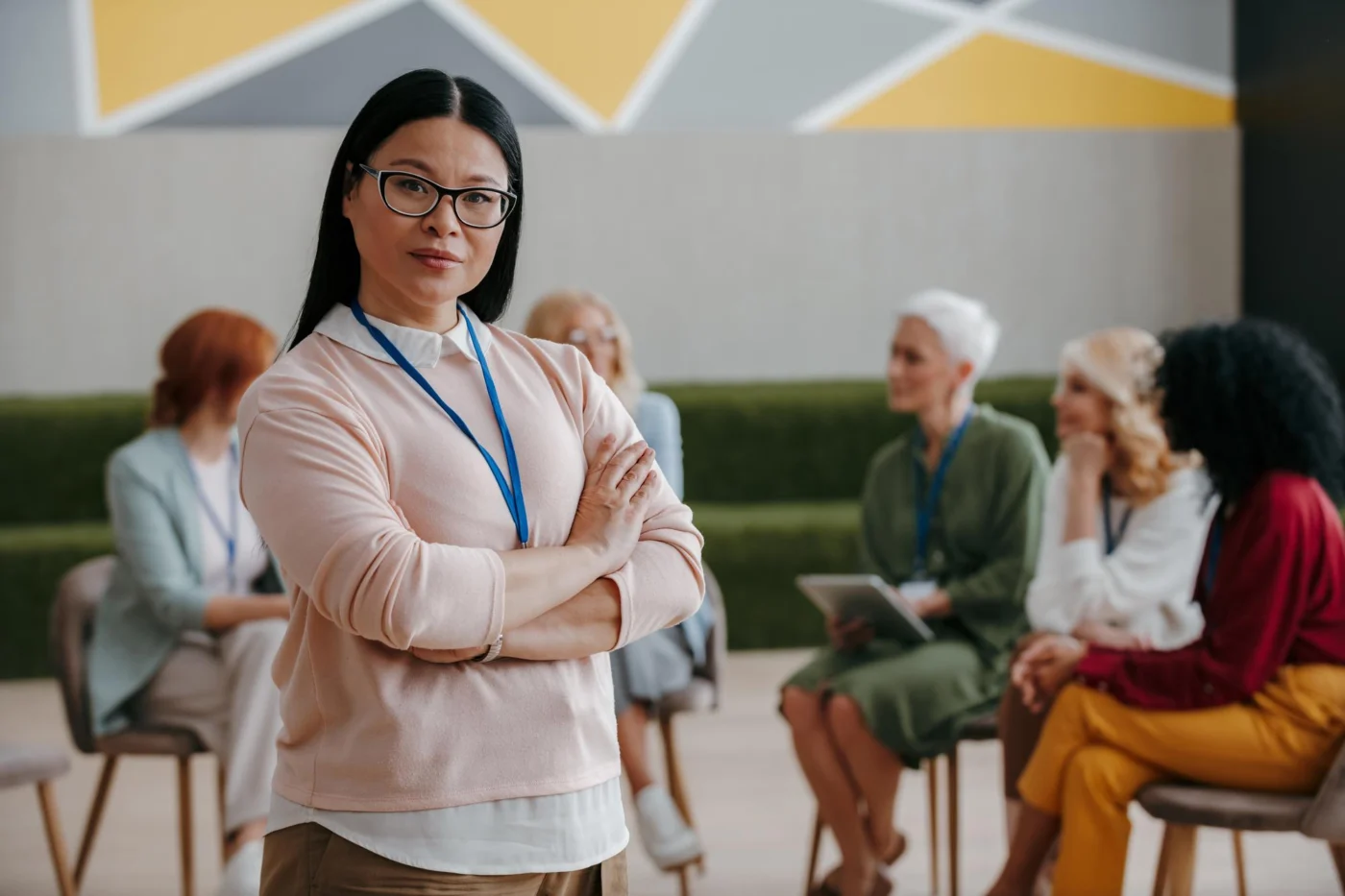Confident woman stood arms folded while a group training session continues behind her